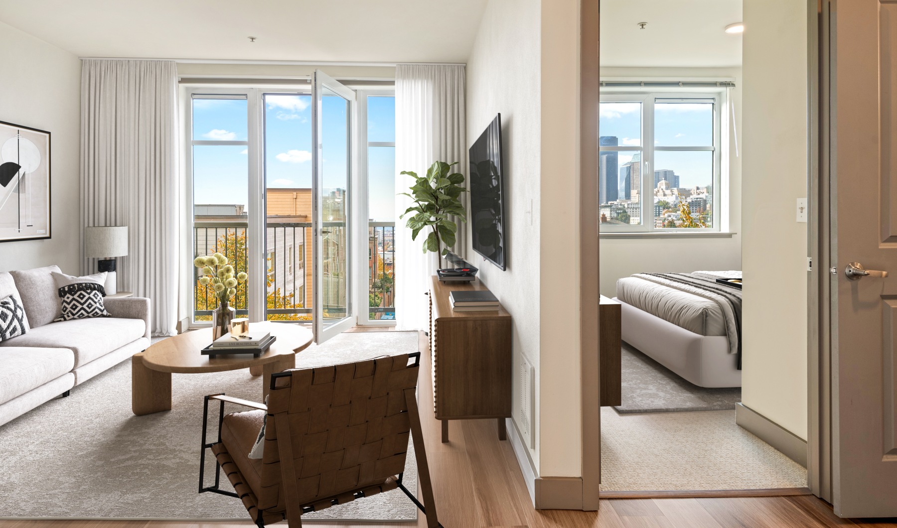 Bright living area with hardwood flooring and open balcony door next to an open doorway revealing a carpeted bedroom with a large window and city view. Description: A bright and airy living space featuring warm hardwood floors and direct access to an outd